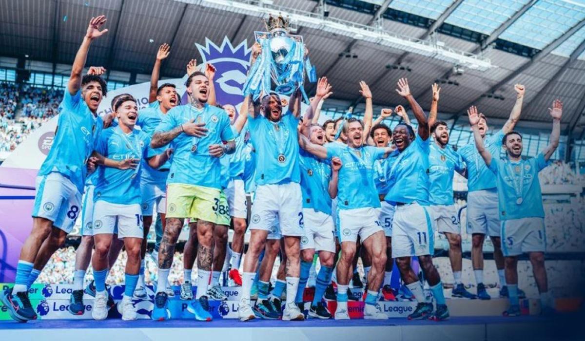 A football team wearing a sky blue kit leaps for joy holding a trophy.