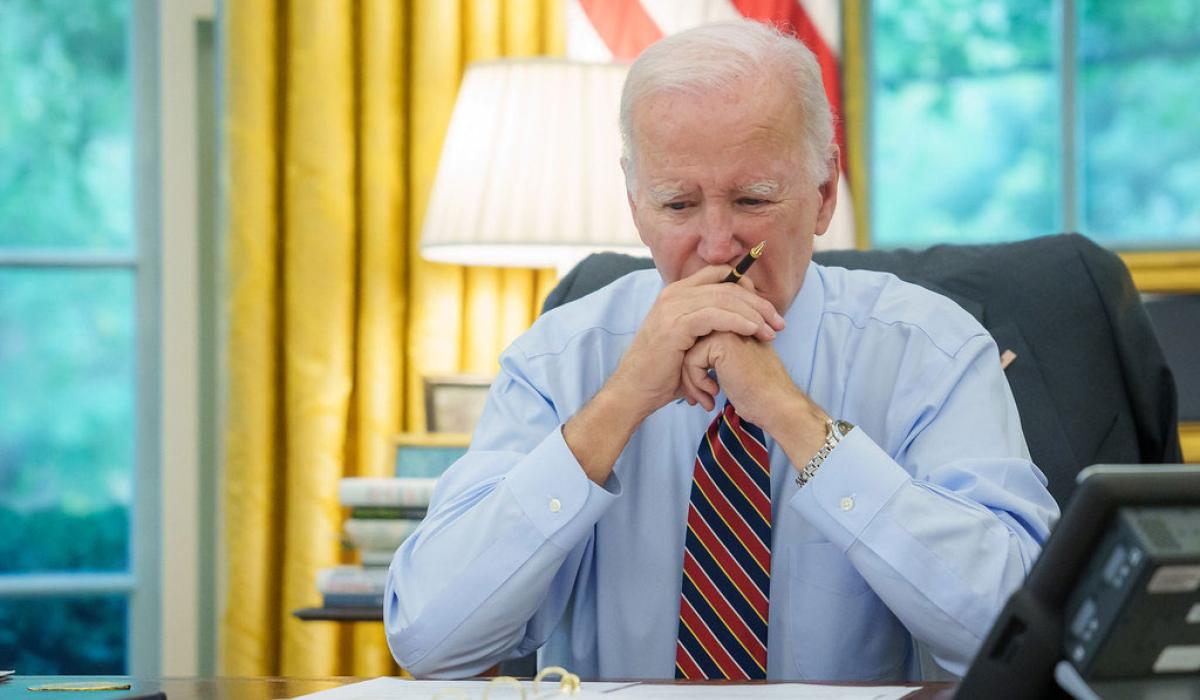 President Biden sits at a desk, holding his balled hands to his mouth.