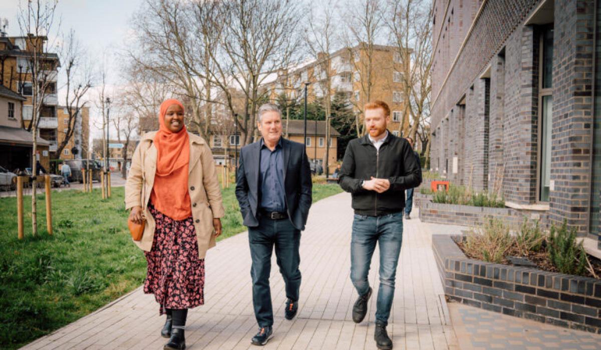 Kier Starmer walks along a residential development's path with two other people.