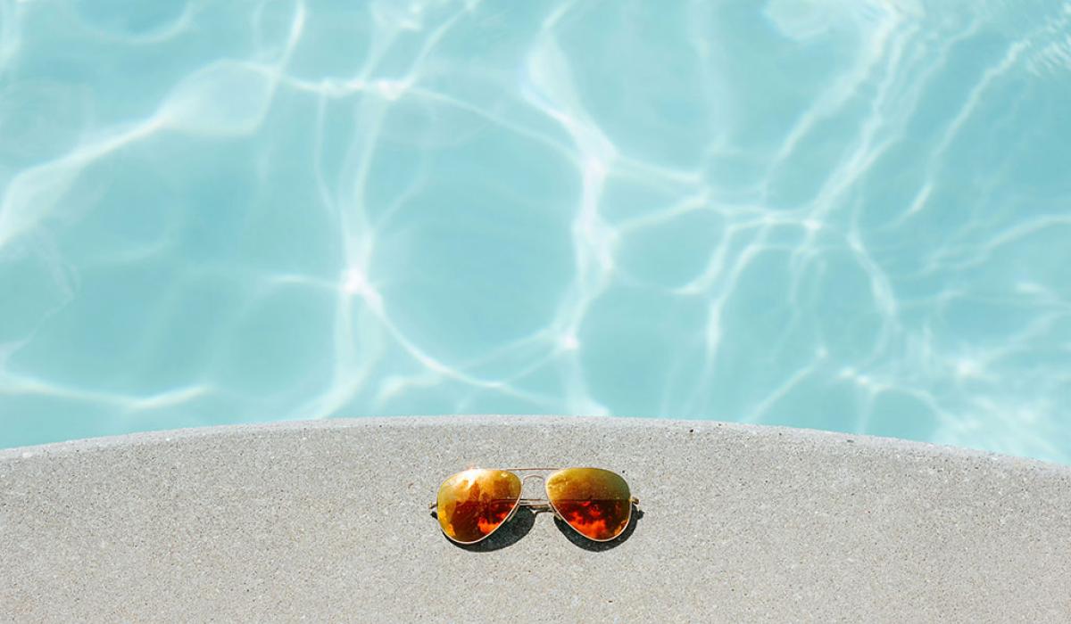 A pair of sunglasses beside a swimming pool.