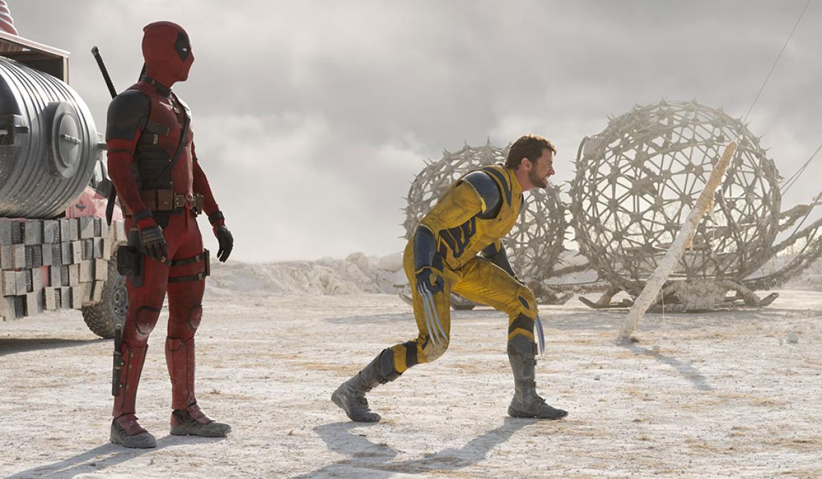 Two superheroes, deadpool and Wolverine, stand and crouch respectively, in a desert like place.