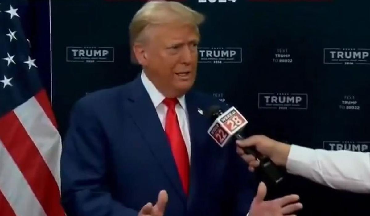 Donald Trump gestures with his hands while someone holds a mic in front of him,