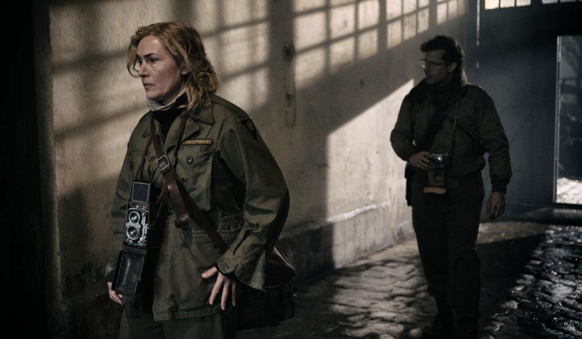 Two war photographers creep along a shadowy corridor.