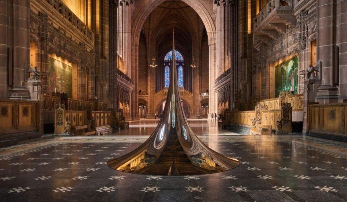 An art structure of a circular peak sits on the chequered floor of a cathedral.