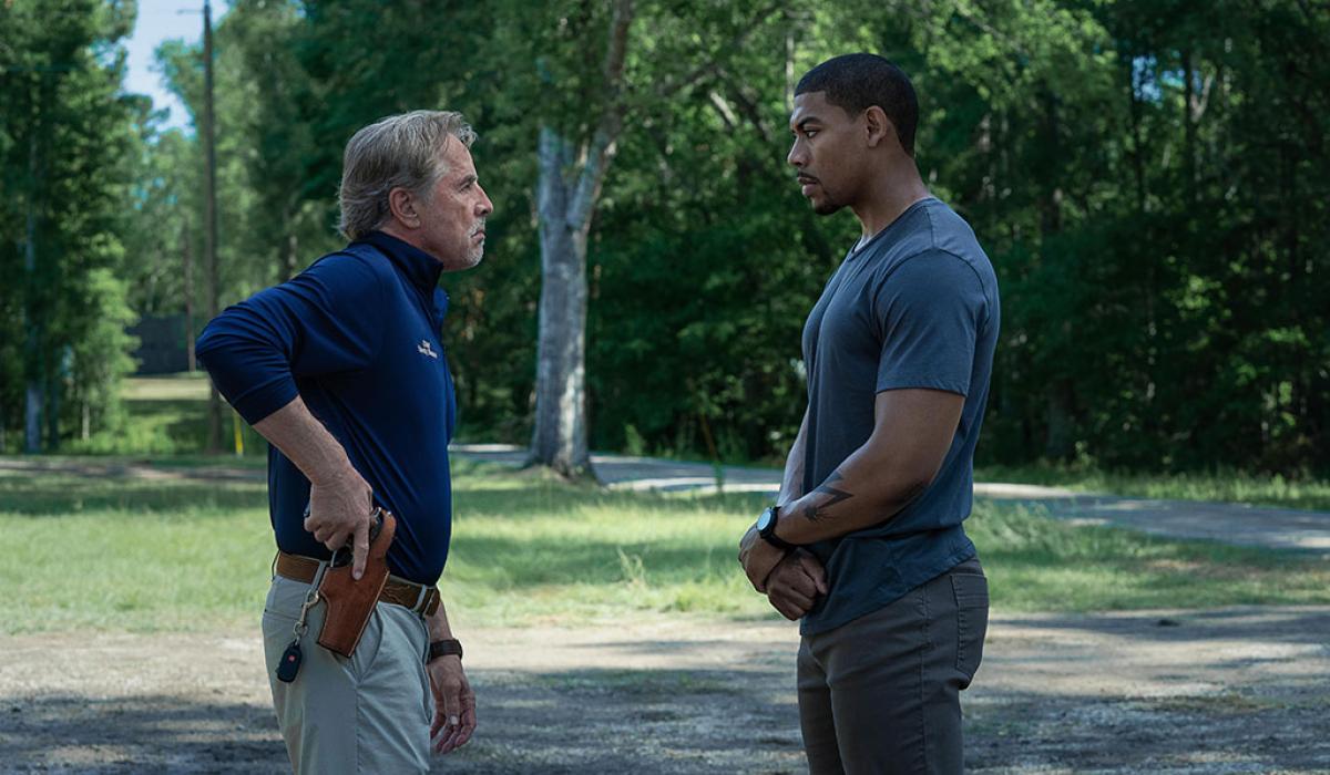 Two men stand off against each other, one holds a holstered gun.