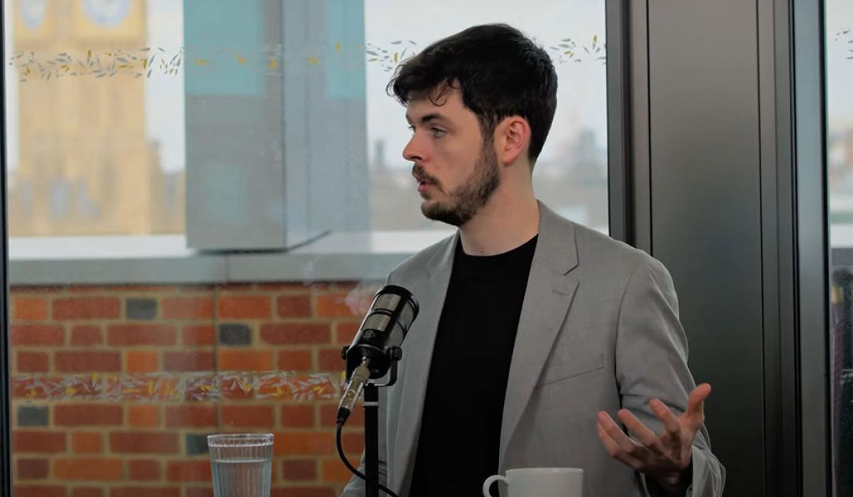 A podcast guest speaks in front of a mic and raises their hand to gesture.