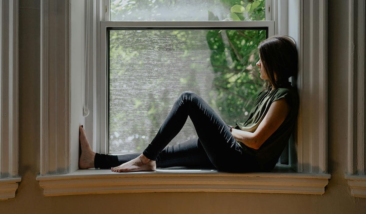 A person sits on a window sill with one raise knee.