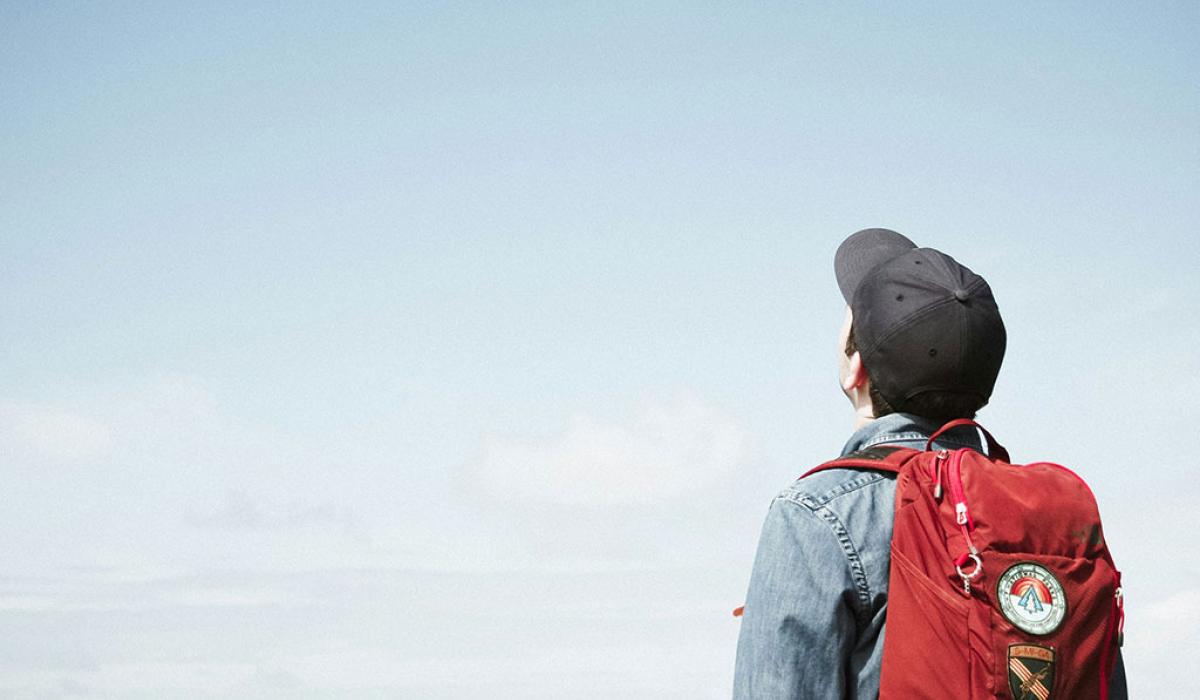 A person wearing a backpack looks to the sky.