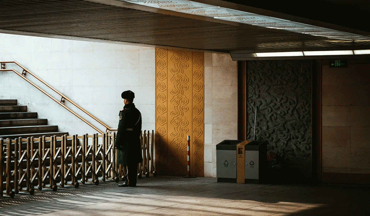 A guard stands behind a barrier across an entrance to a station escalator.