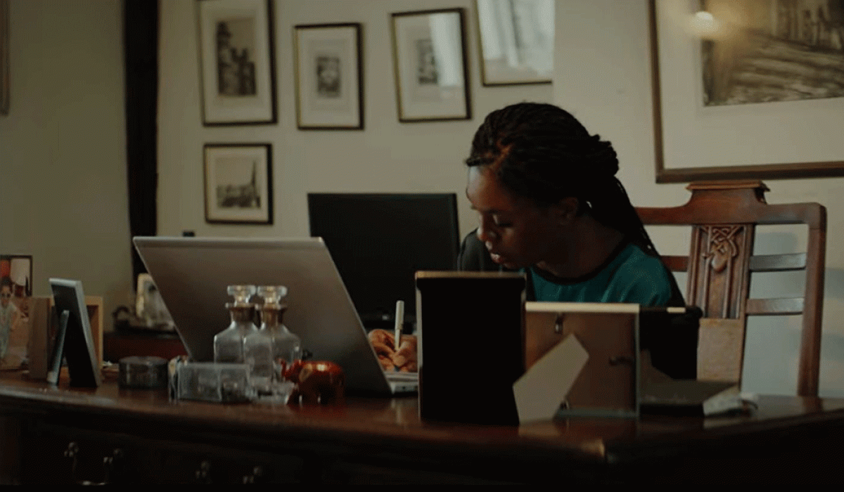 A woman works at a laptop on a desk surrounded by picture frame.