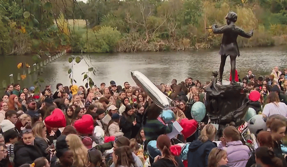 A crowd of teenagers gather by a Peter Pan statue to mourn a dead pop star