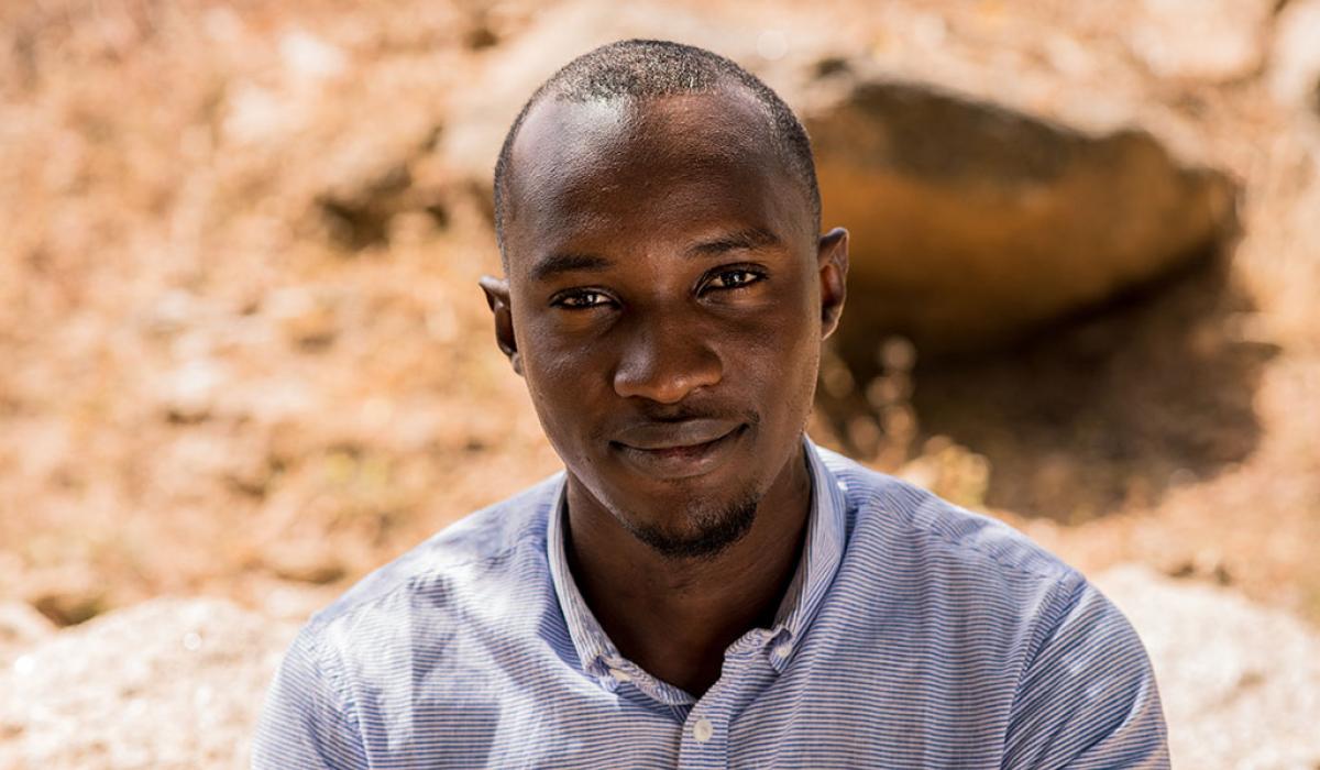 A Nigerian man looks up towards the camera, behind him is dusty ground