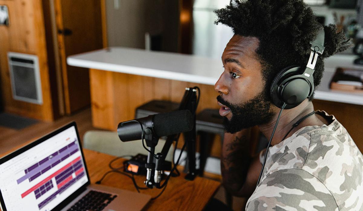 A podcaster speaks into a mic before a screen.