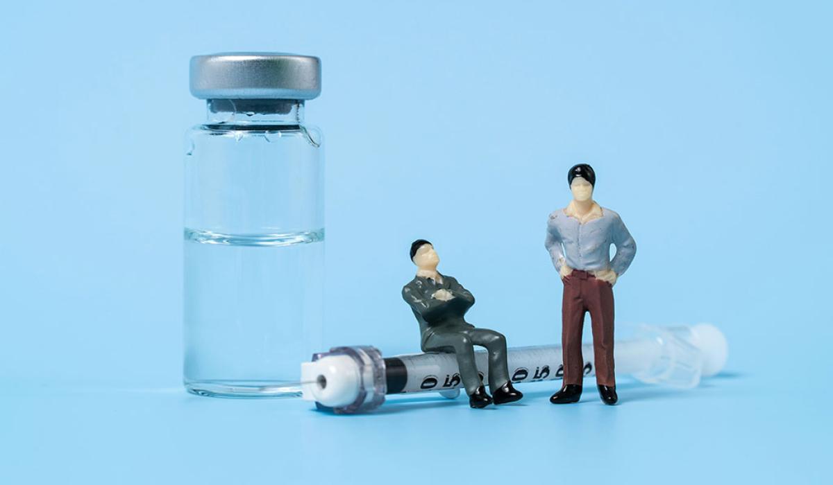 A tableau shows minature figures of two people, one sitting on a life size syringe and the other stands