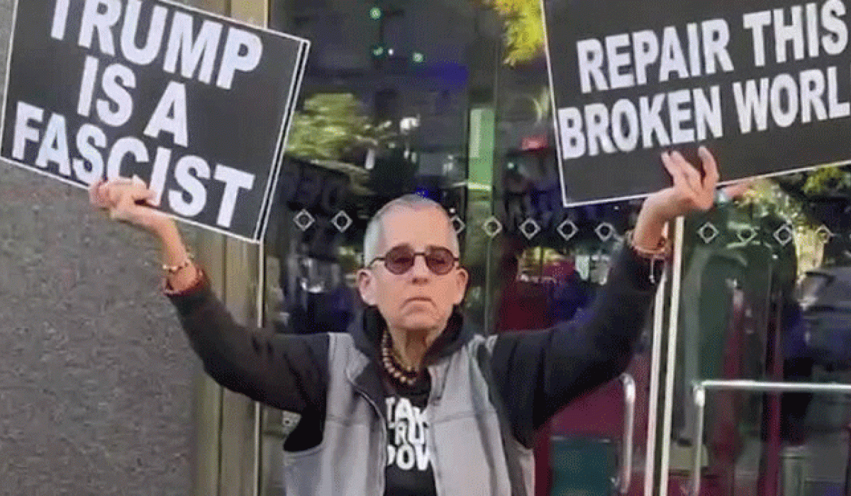 A protester holds placards up in both hands. One reads: Trump is a fascist. The other: Repair the broken world 