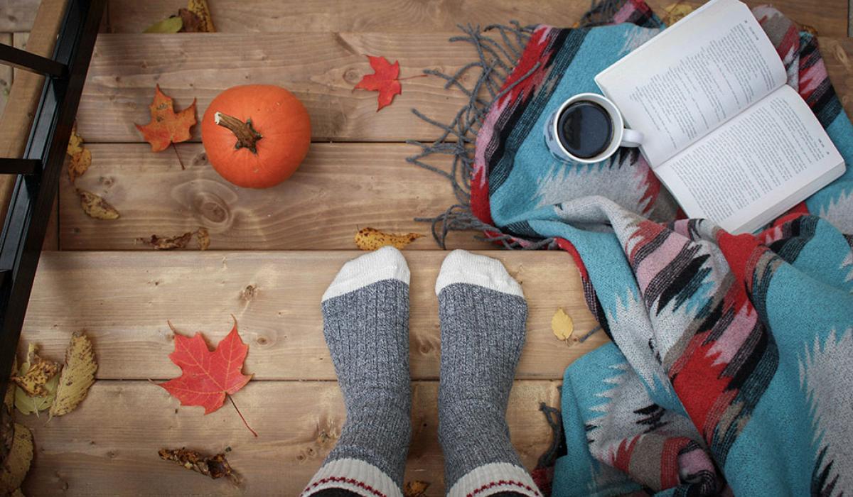 A set of be-socked feat rest on a leaf strewn step beside a book and a cup of coffee.