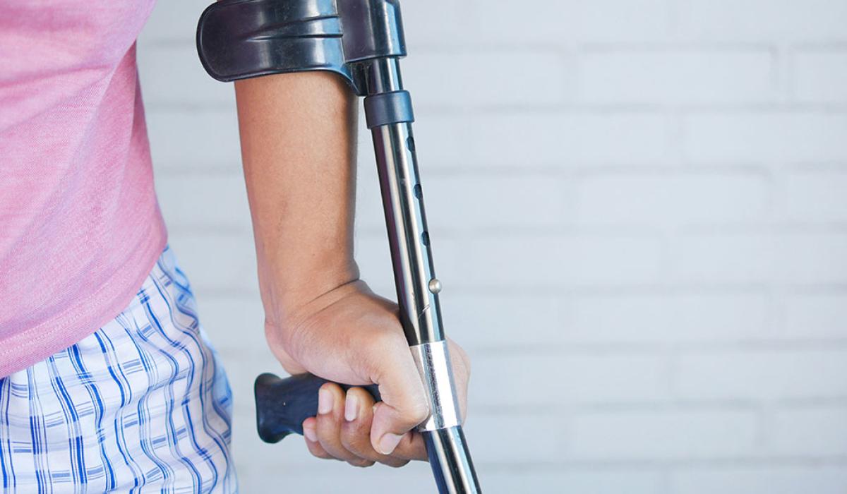 A crutch is held in the hand of someone in pyjamas.