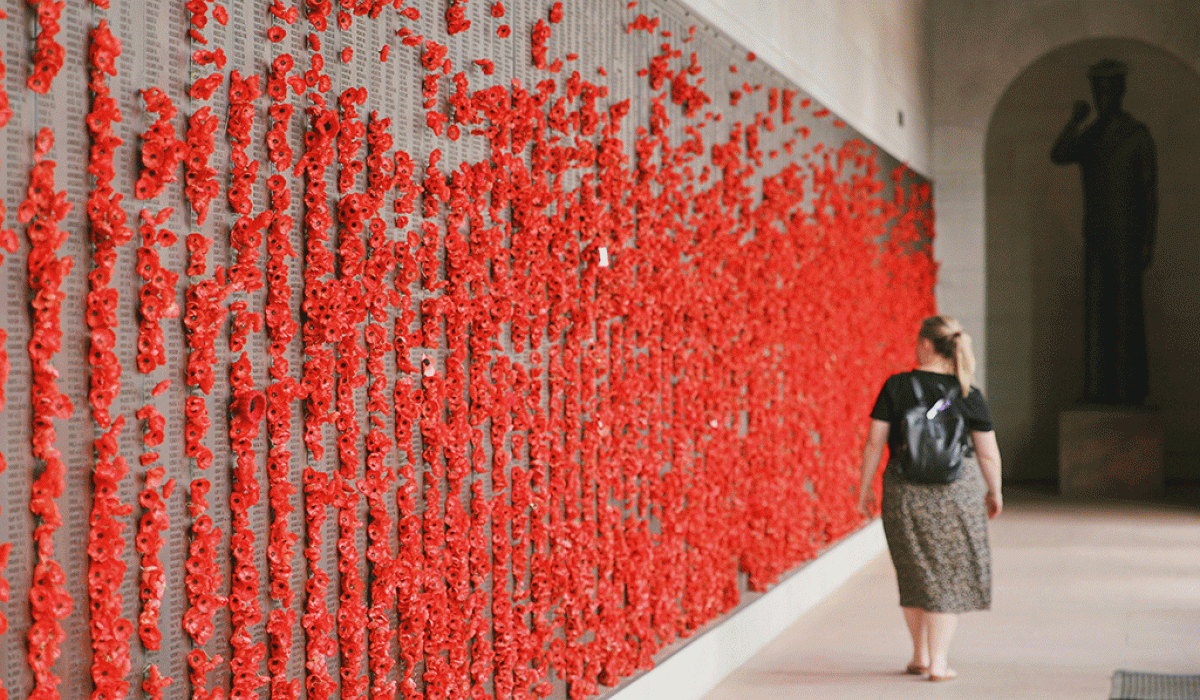 A woman walls along a war memorial wall covered in red poppies.