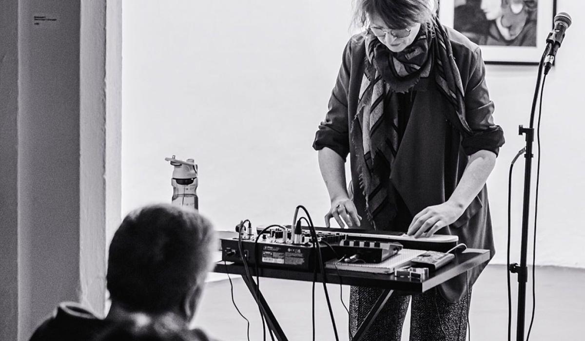 A woman stand at a mixing desk playing a small keyboard.