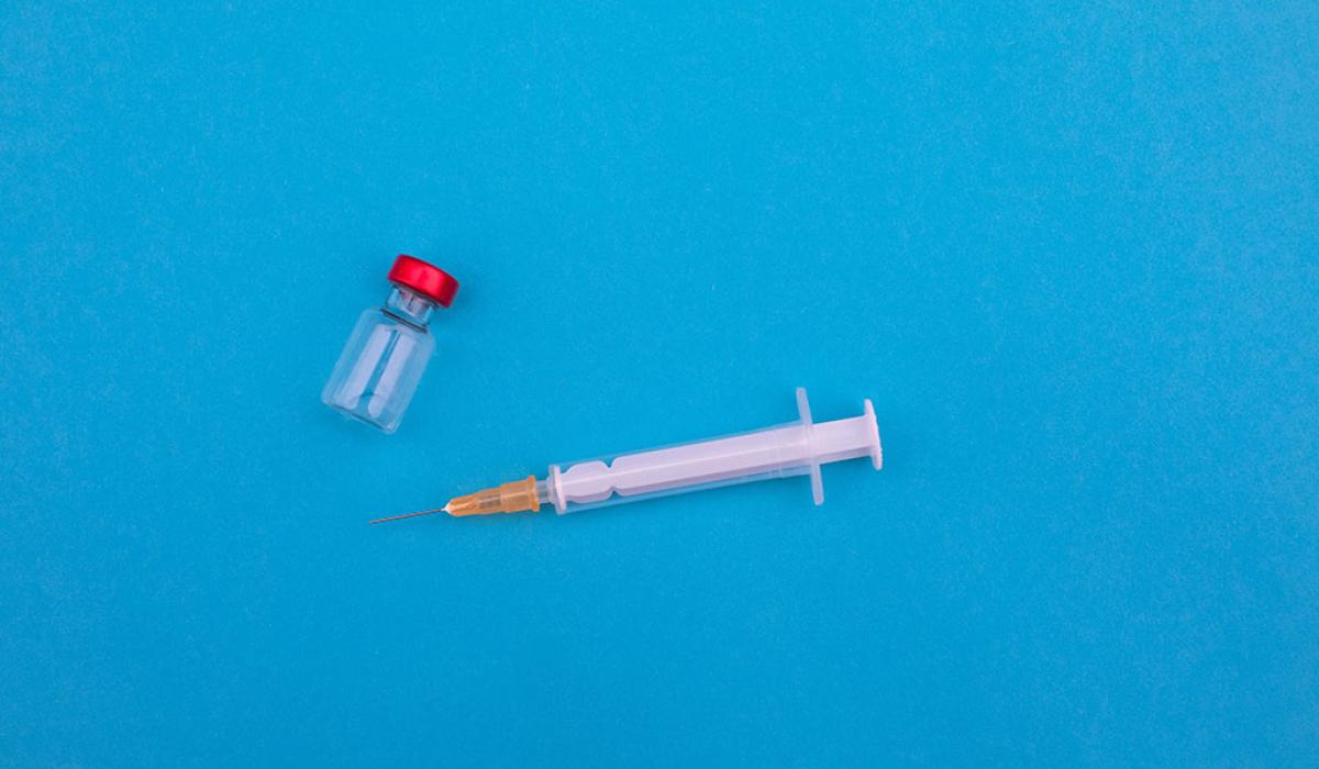 A vial and syringe lie on a blue backdrop.