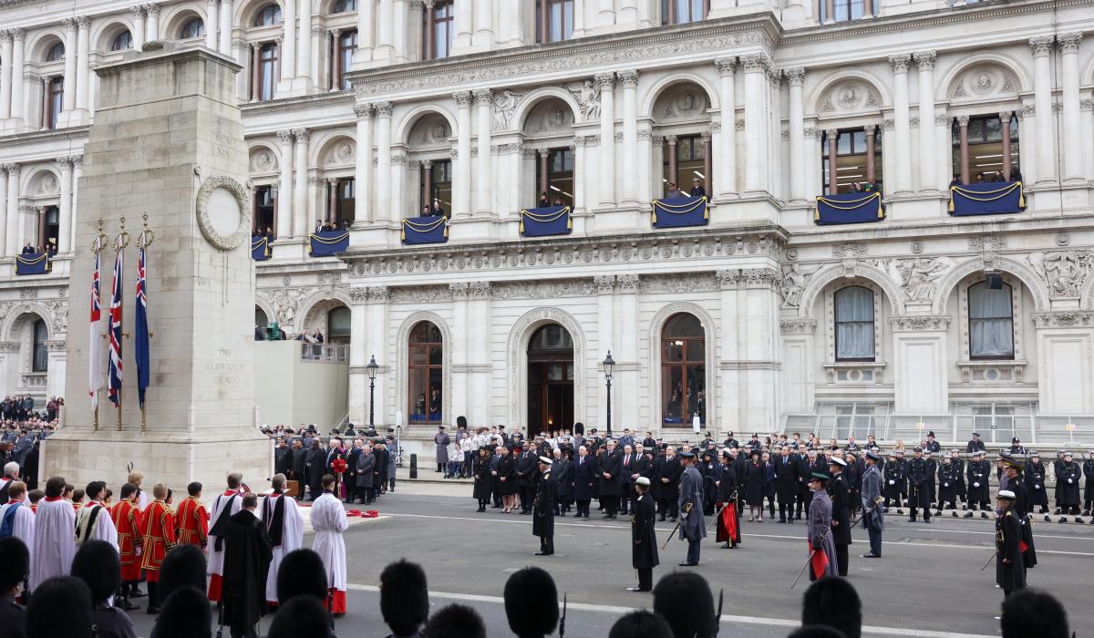 A Remembrance Sunday service stands to attention around a cenotaph.