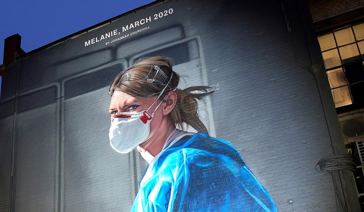 A gable end mural depicts a nurse in scrubs and a mask turning and looking towards the viewer.