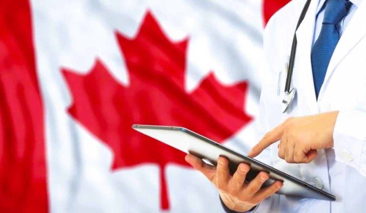 a doctor consults a tablet against the backdrop of a Canadian flag.