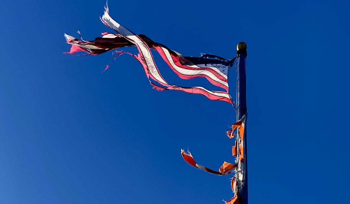 a tattered American flag flies against a blue sky.