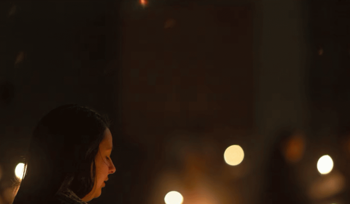 A carol singer looks down while candles flicker.