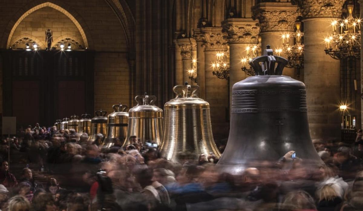 Restored church bells lined up in a cathedral, as crowds mill around them.