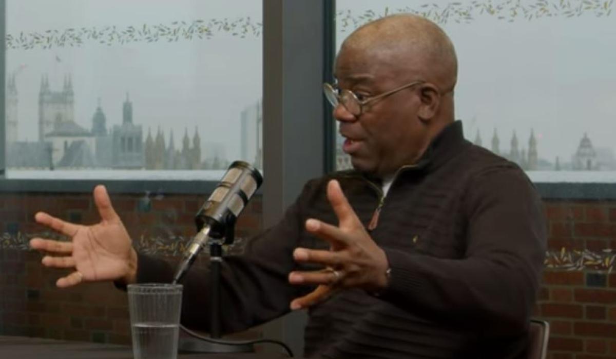 A podcast guest talks in front of a mic, while gesturing with both hands.