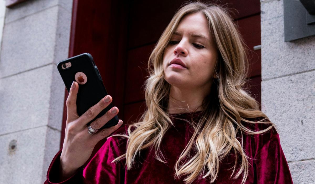 A woman holds her phone up in her hands and looks at it in a slightly vexed way.