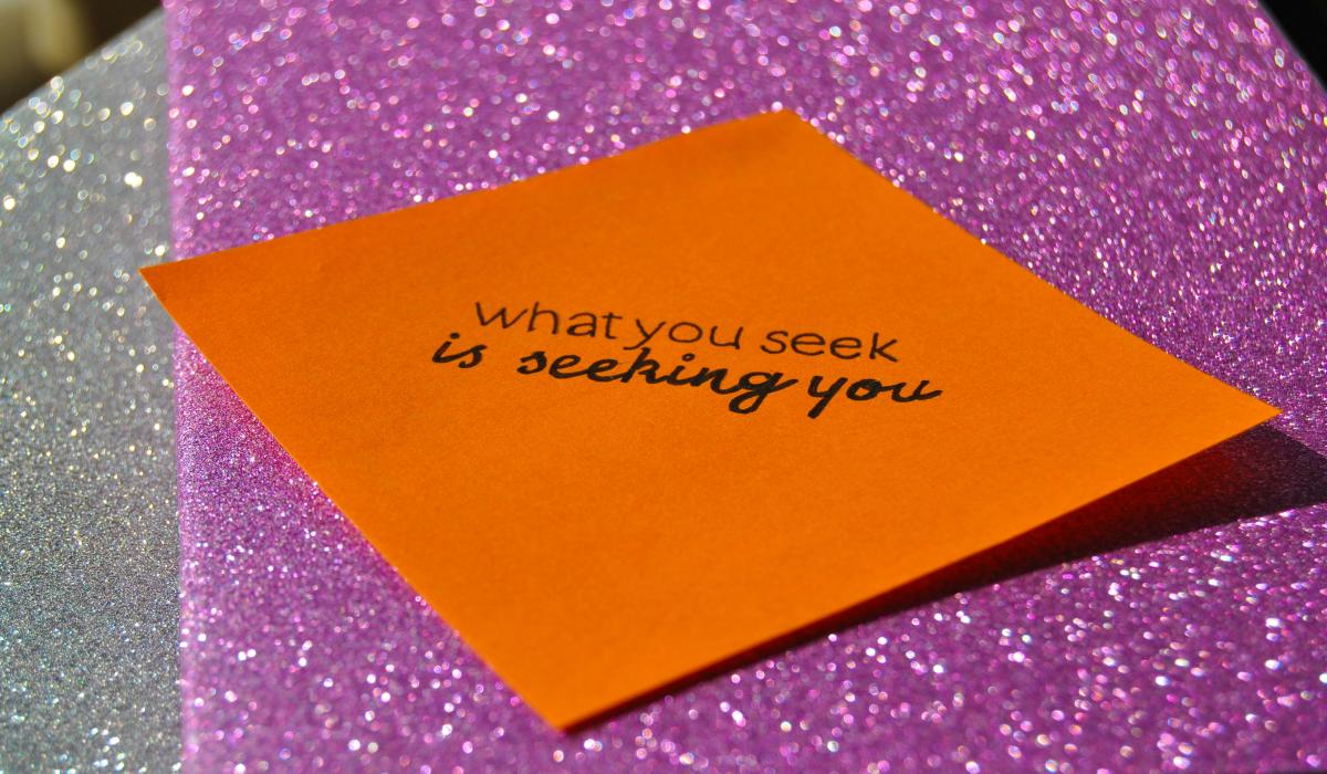 Against a purple glittery background, a orange notelet reads: 'what you seek is seeking you.'