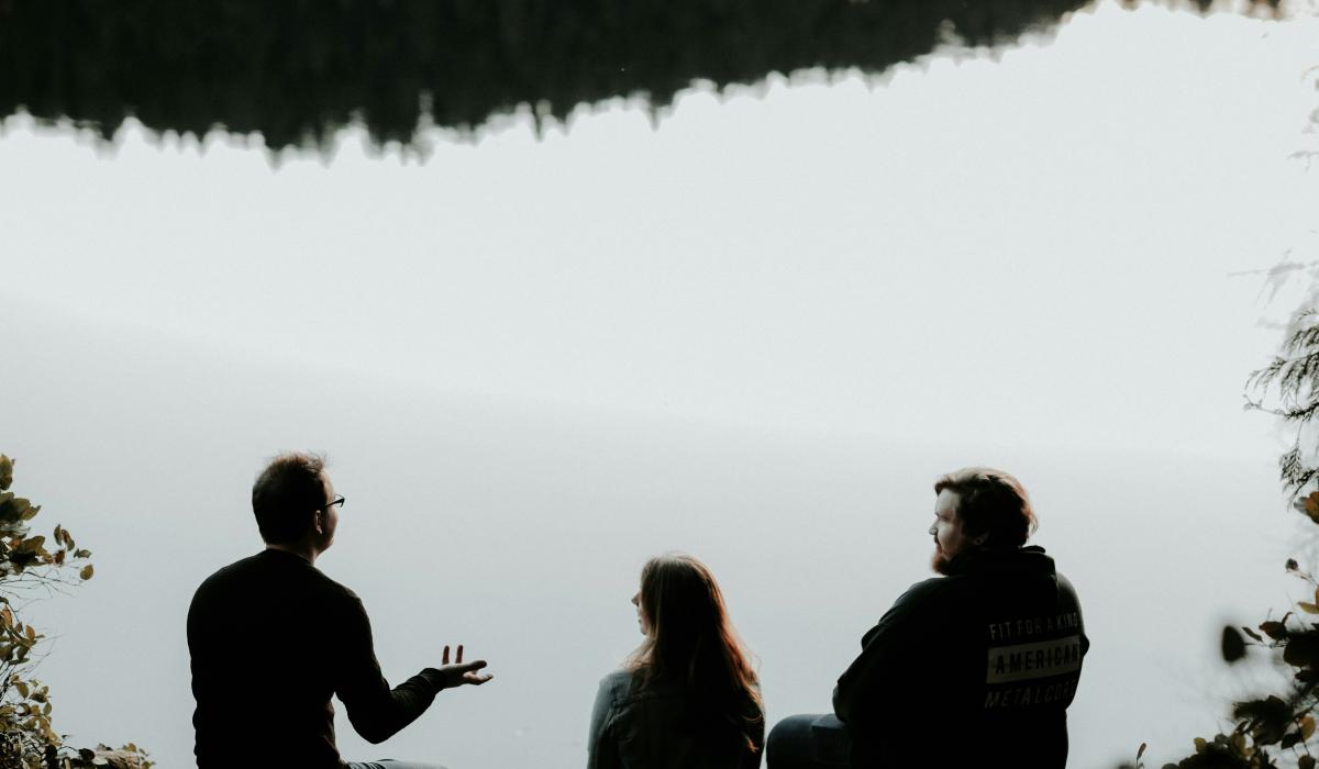 Three people sitting looking out over viewpoint are silhouetted against the sky. 