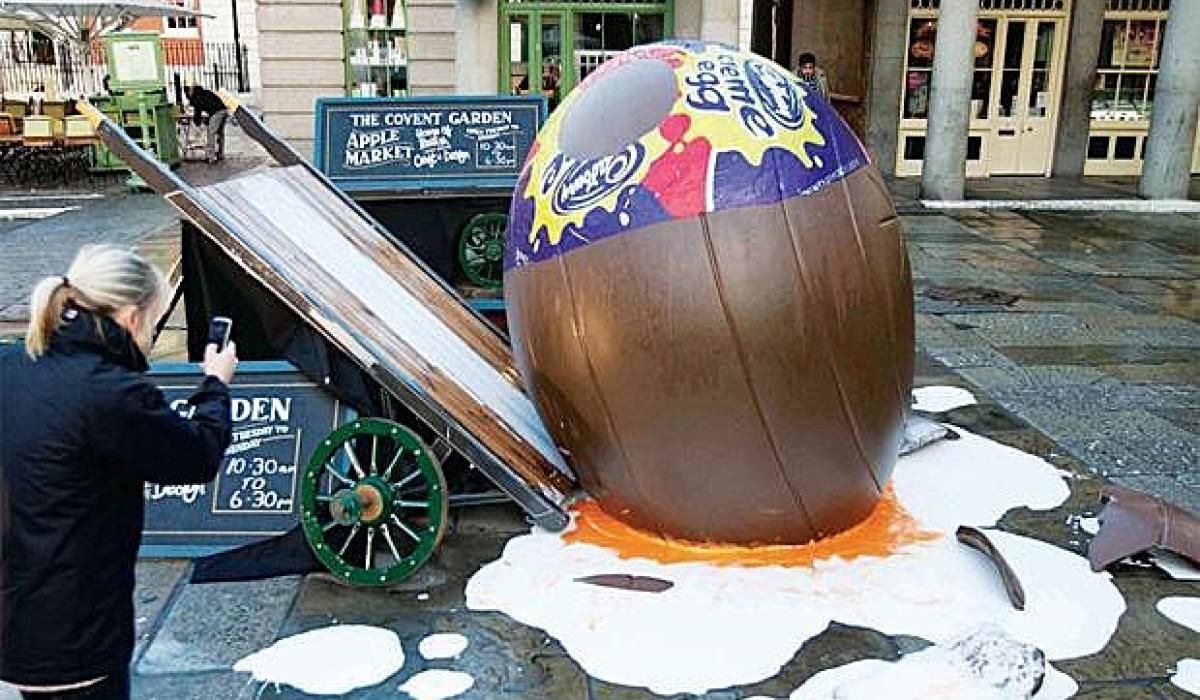 A giant creme egg lies smashed on the ground beside a tilted market barrow.