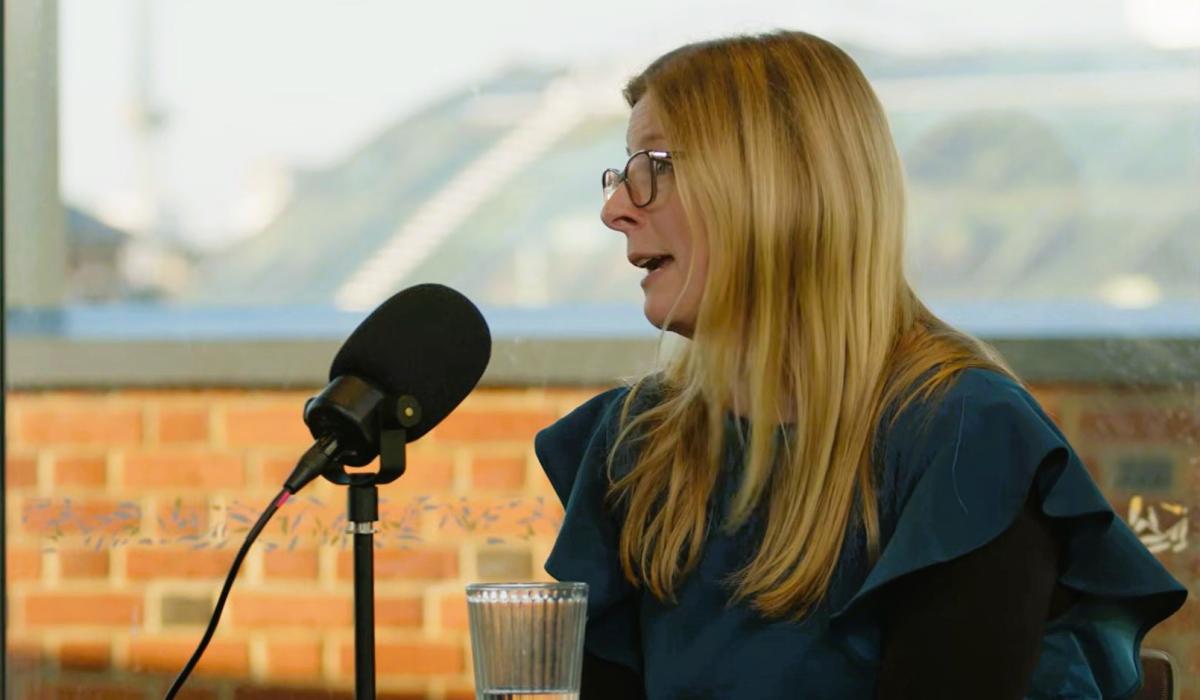 A woman sits at a table and talks with a microphone on a stand in front if her,