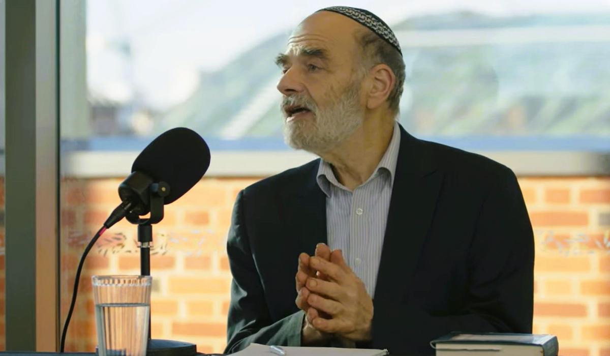 A podcast guest holds his hands together in front of himself as he raise his head in speech.