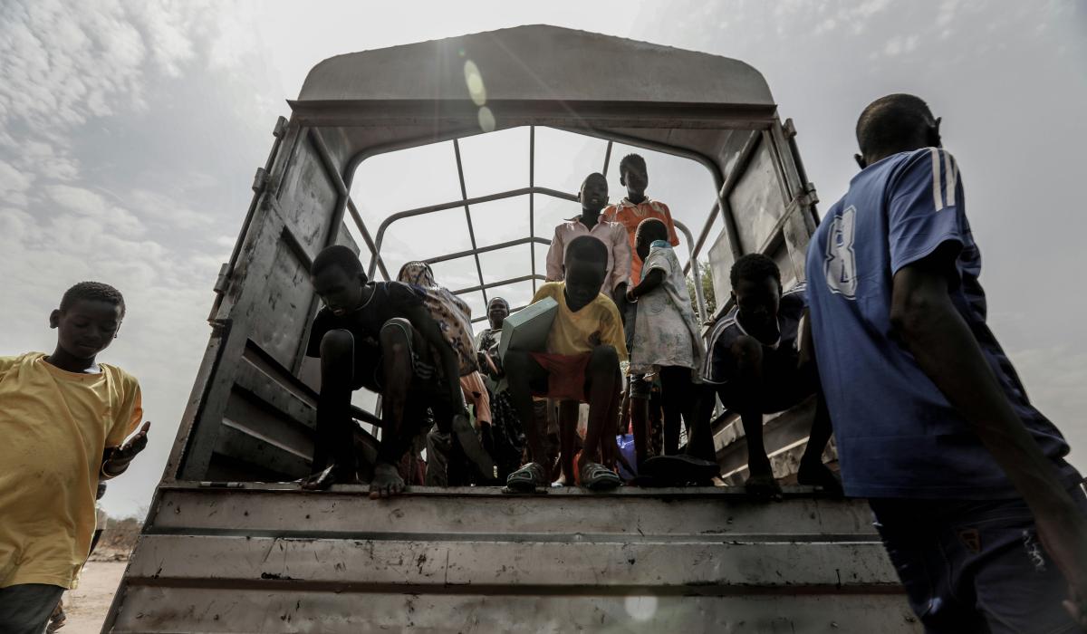 Refugees stand at the back of an open truck.