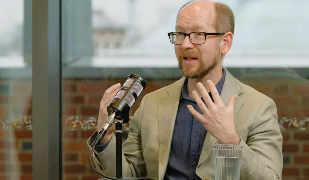 A podcast guest sits in front of a mic, gesturing with their hands.