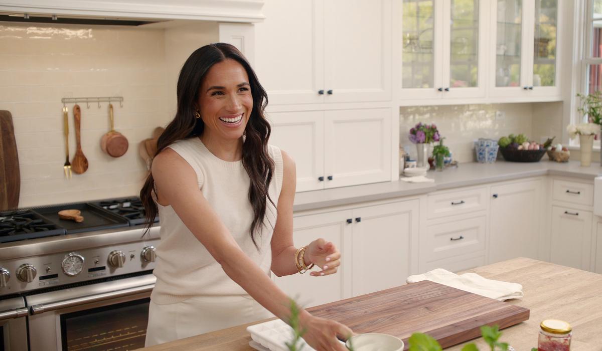 A woman stands at a kitchen island with a chopping board on it.