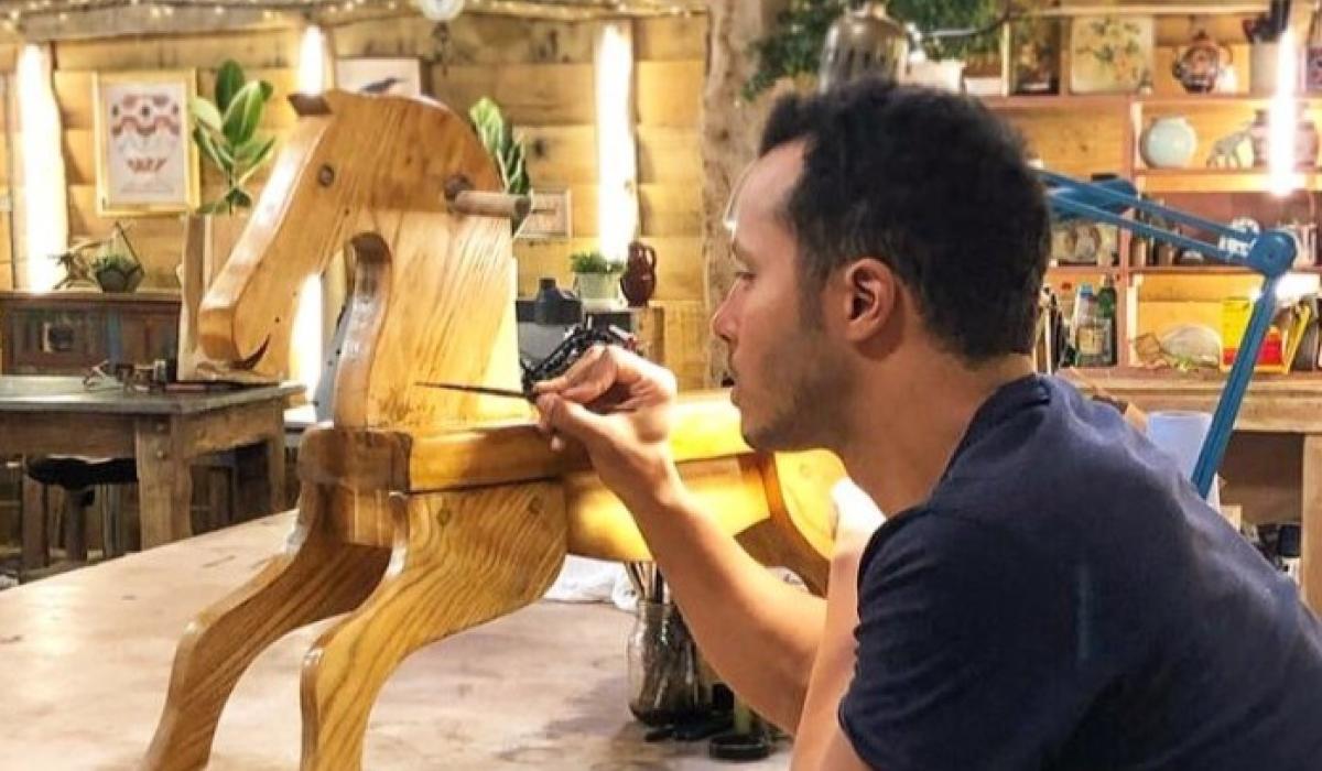 A restorer rest on his elbows while painting a wooden rocking horse.