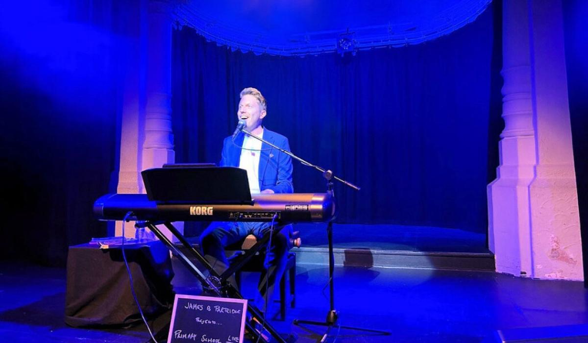 A pianist sits at a keyboard singing on a stage.