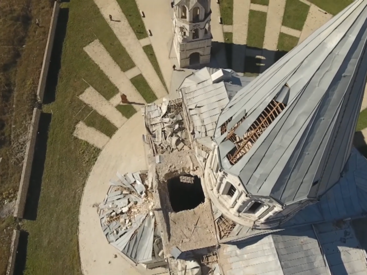 An aerial view looking down the damaged spire of a cathederal to a holes in the roof caused by shelling.