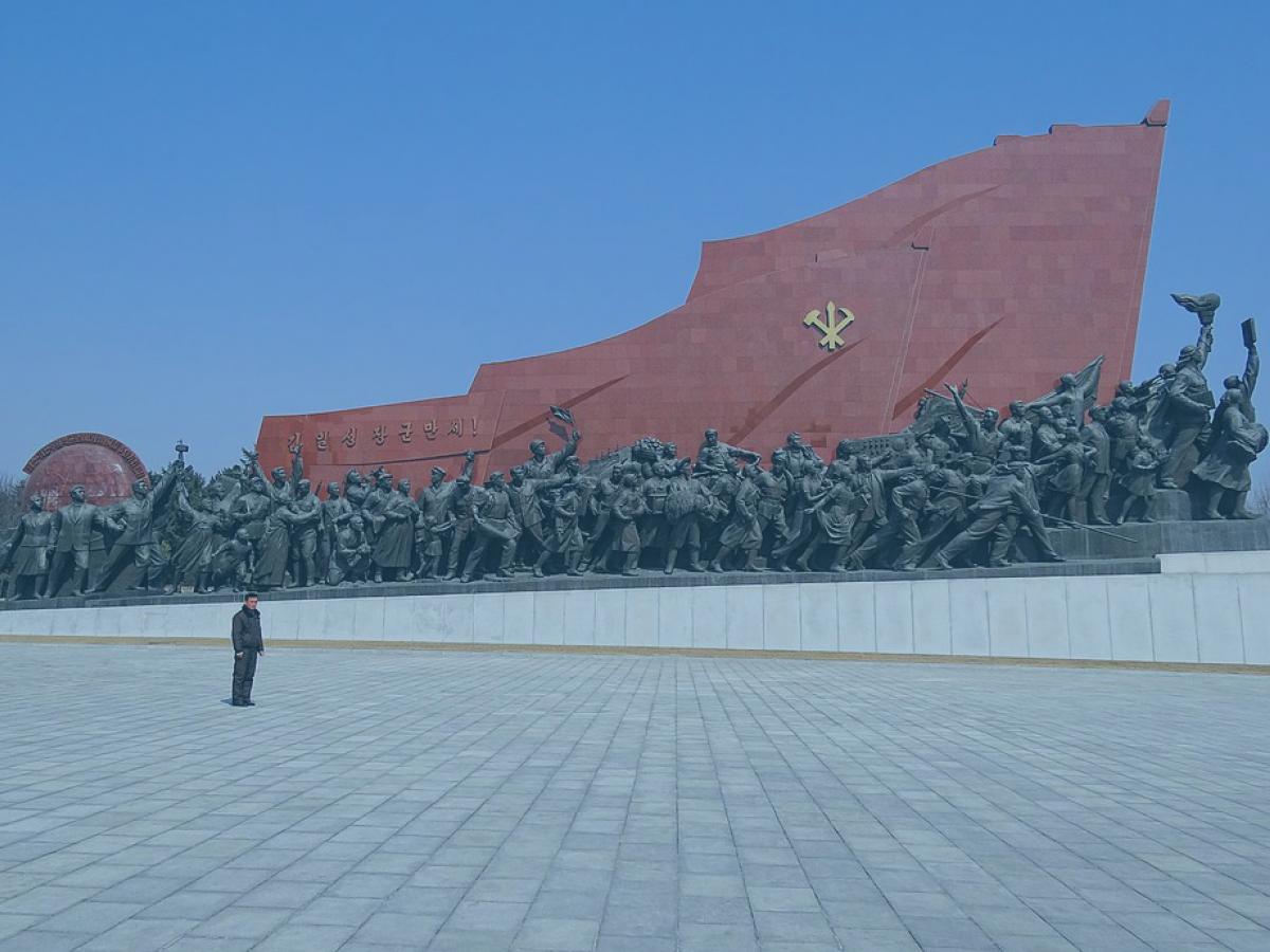 A huge communist monument consists of a red flag wall rising from left to right over a column of statues.