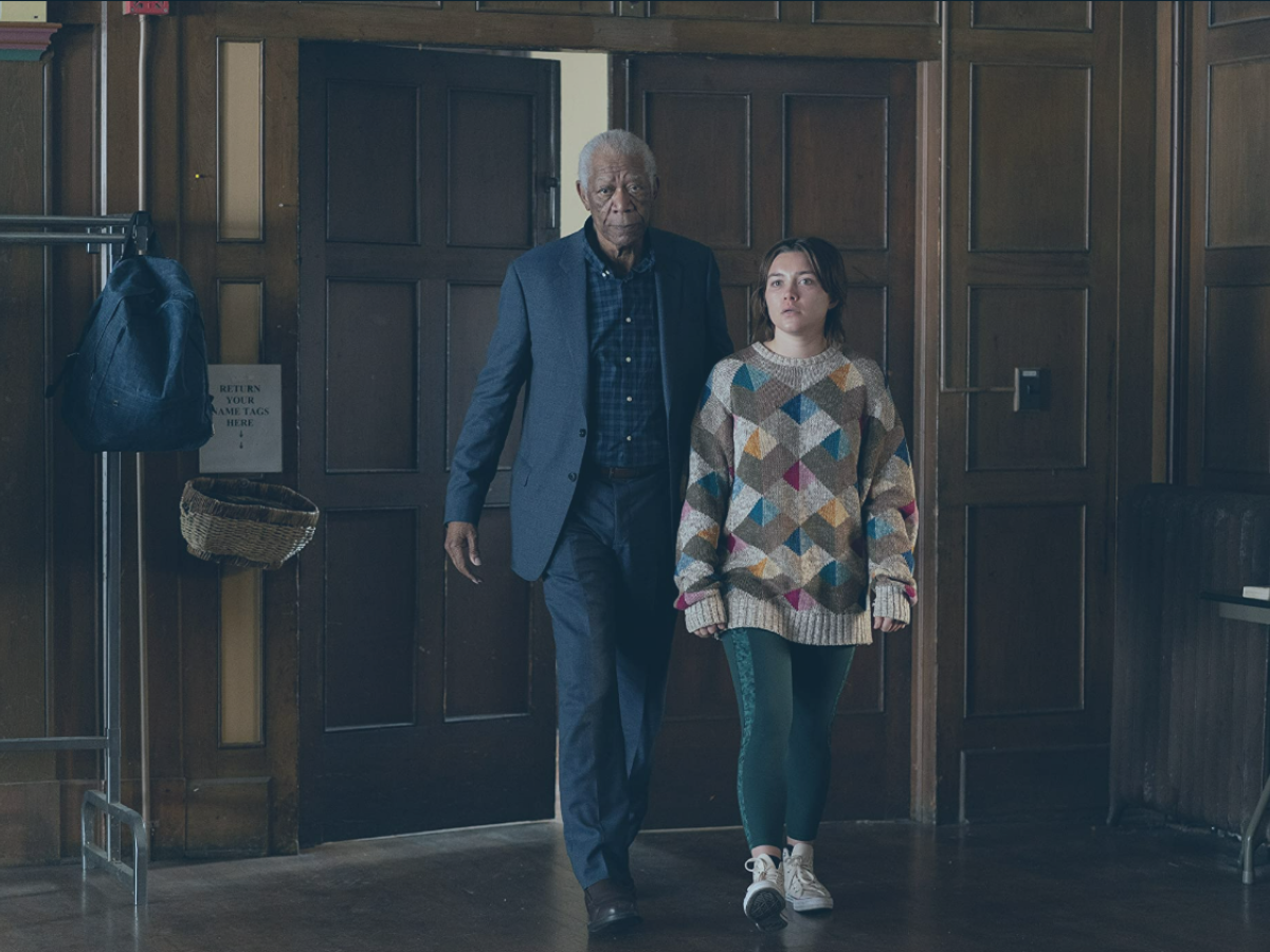 An old man accompanies a young woman into a wood-panelled hall, both look aprehensive.