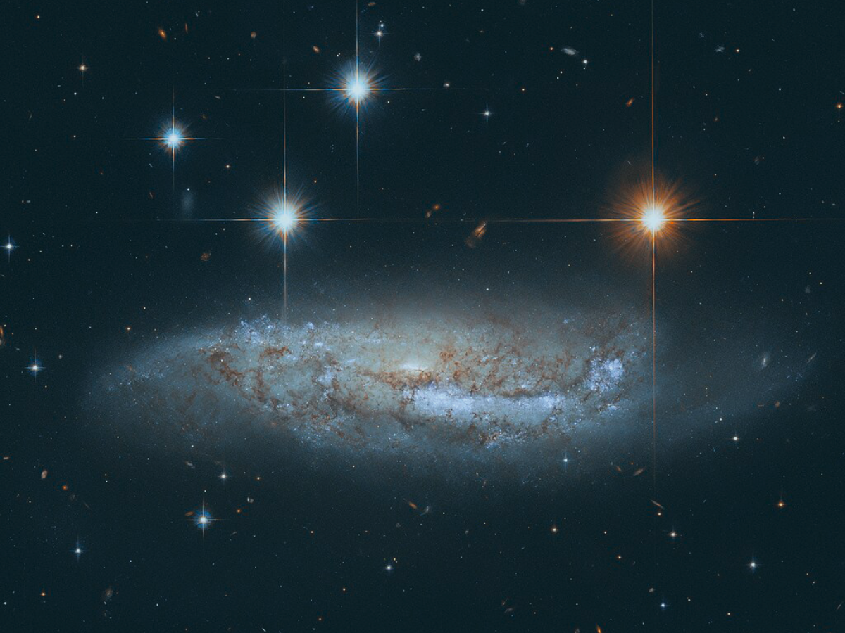 Four stars scintilate above a spiral galaxy viewed from the side.