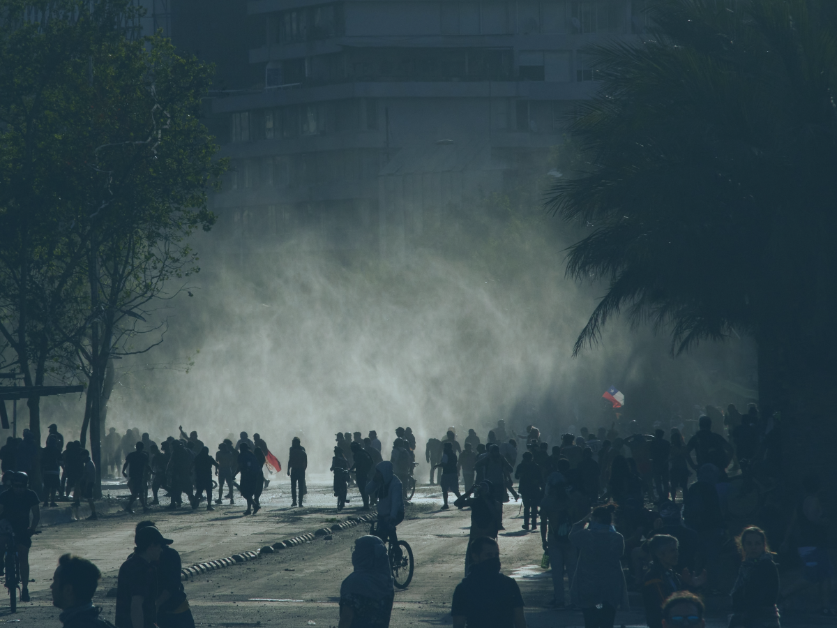 A loose rabble of a protest in the street is siluhetted against light and a shower of rain