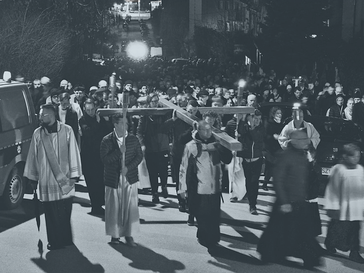 A Good Friday procession of people and priests hold a cross horizontal above their heads.