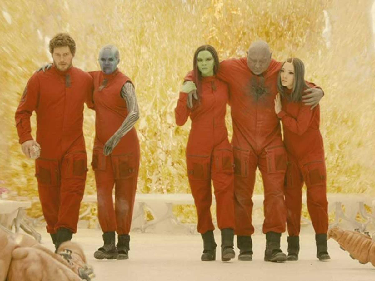 Five people in red jump suits help each other stand together.