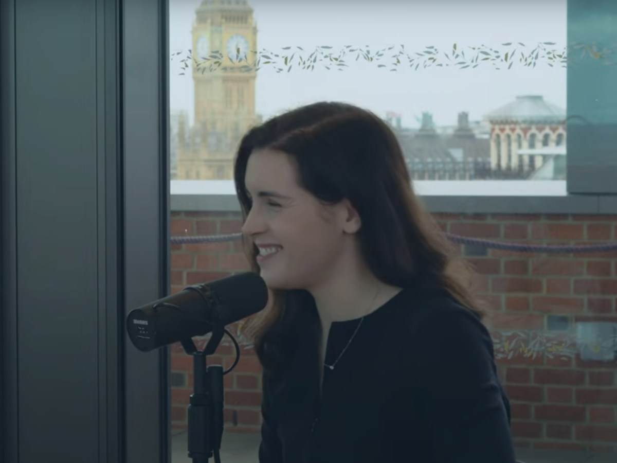 A woman smiles as she speaks into a microphone. In the background is Big Ben.